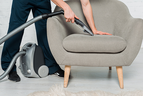 cropped view of cleaner in uniform dry cleaning armchair with vacuum in modern living room