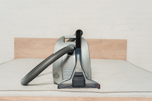 modern vacuum cleaner with handle on mattress in bedroom