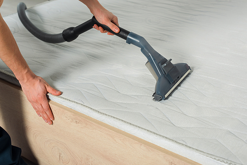 cropped view of cleaner removing dust on mattress with vacuum cleaner