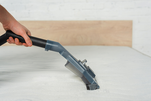 cropped view of cleaner removing dust on mattress in bedroom with vacuum cleaner