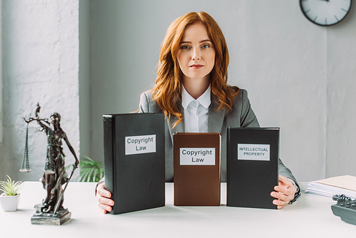 Redhead lawyer  and holding books with copyright law and intellectual property lettering, while sitting at table