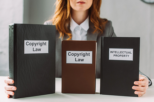 Cropped view of lawyer holding book with intellectual property and copyright law lettering on table on blurred background