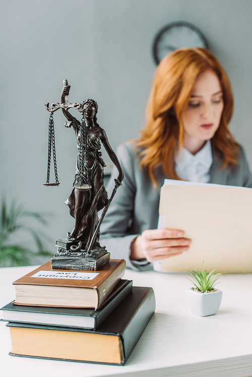 Themis figurine on pile of books on table with blurred female lawyer on background