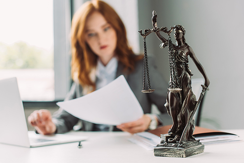 Themis figurine on table with blurred lawyer working on background