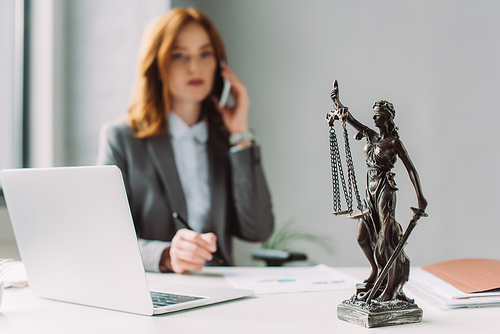 Themis figurine on table with blurred lawyer talking on mobile phone on background