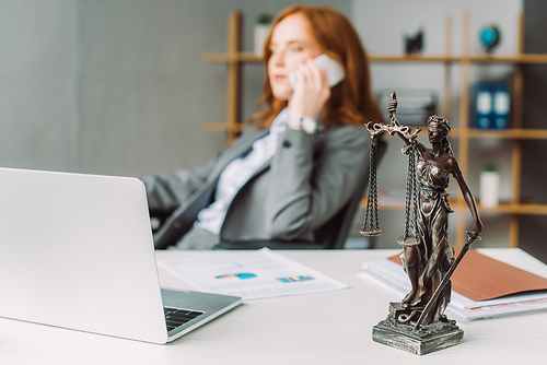 Themis figurine on table near laptop with blurred female lawyer talking on phone on background