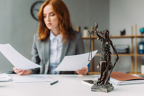 Themis figurine on table with blurred lawyer with paper sheets on background