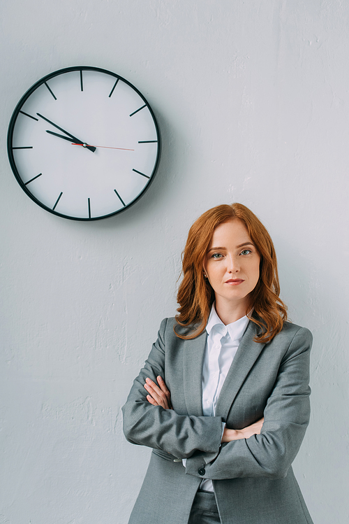 Front view of confident businesswoman with crossed arms  near wall clock on grey
