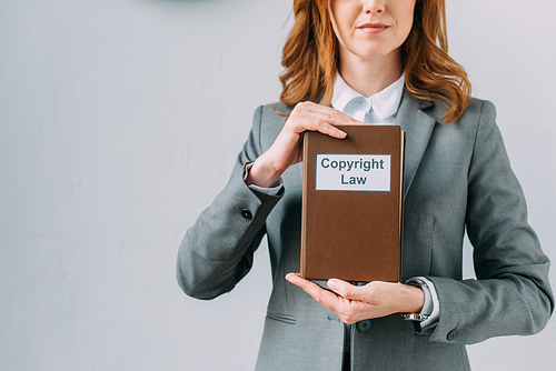 Cropped view of female lawyer showing book with copyright law lettering on grey