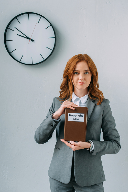 Front view of businesswoman , while showing book with copyright law lettering near wall clock on grey