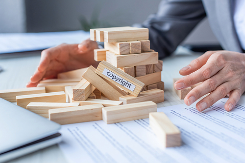 Cropped view of lawyer holding hands near blocks wood game construction with copyright lettering collapsing on blurred background