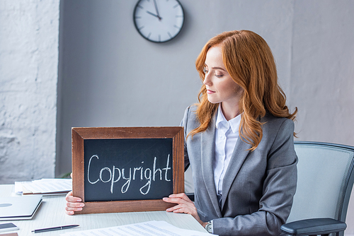 Female lawyer showing chalkboard with copyright lettering, while sitting at workplace on blurred background