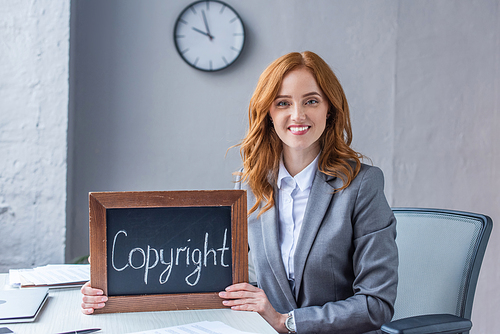Smiling female lawyer , while showing chalkboard with copyright lettering at workplace on blurred background