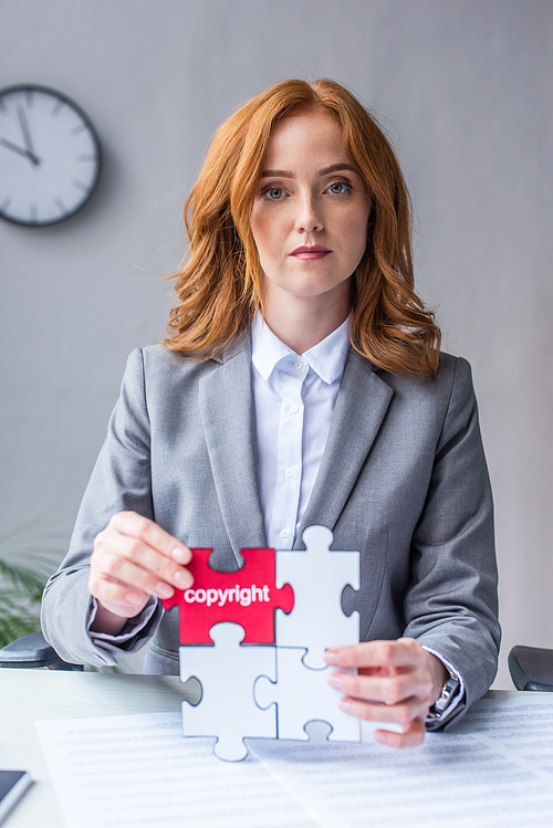 Serious lawyer , while showing jigsaw puzzles with copyright lettering at workplace on blurred background