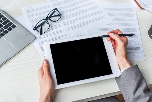 Cropped view of businesswoman holding pen near digital tablet near documents on table
