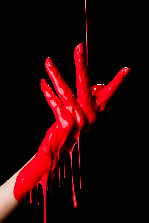 partial view of painted hand with red dripping paint isolated on black
