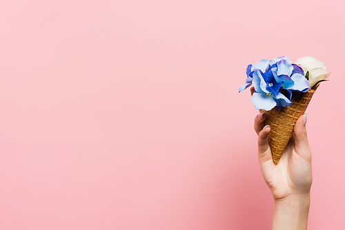 cropped view of woman holding waffle cone with blue flowers isolated on pink