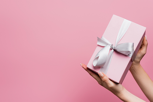 partial view of woman holding wrapped present isolated on pink
