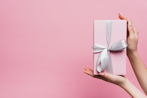partial view of woman holding wrapped present in hands isolated on pink