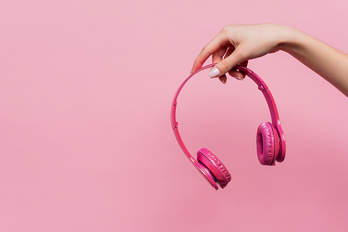 partial view of woman holding wireless headphones in hand isolated on pink