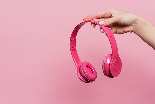 partial view of woman holding wireless headphones isolated on pink