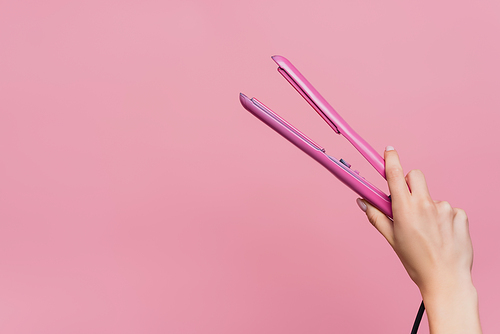 partial view of woman holding hair straightener in hand isolated on pink