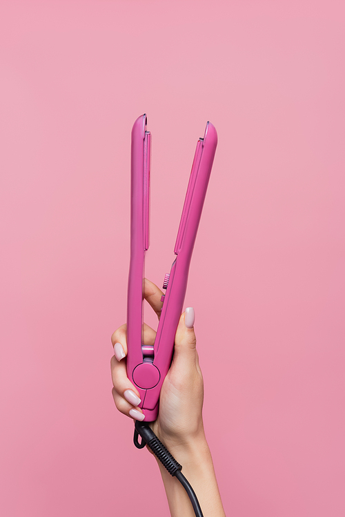 cropped view of woman holding hair straightener isolated on pink