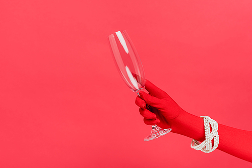 cropped view of woman in glove holding empty champagne glass isolated on red