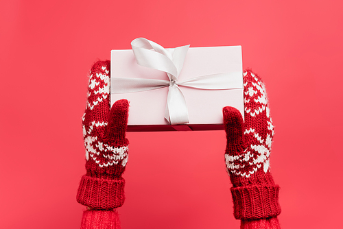 cropped view of woman in mittens holding gift box isolated on red