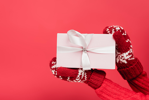 cropped view of woman in mittens holding wrapped present isolated on red