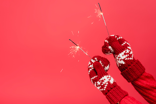cropped view of woman in mittens holding sparklers isolated on red