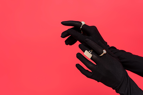 cropped view of female hands in black gloves with golden rings isolated on red
