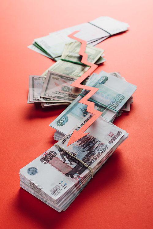 selective focus of paper cut recession arrow on ruble, dollar and euro banknotes on red background