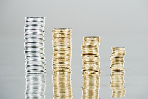 stacks of silver and golden coins on surface with reflection isolated on grey