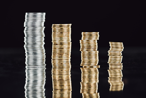 stacks of silver and golden coins on surface with reflection isolated on black