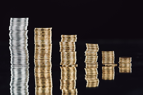 stacks of silver and golden coins on surface with reflection isolated on black