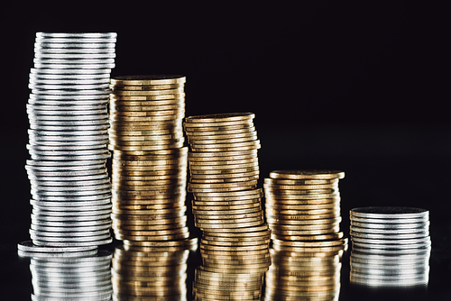 stacks of silver and golden coins on surface with reflection isolated on black