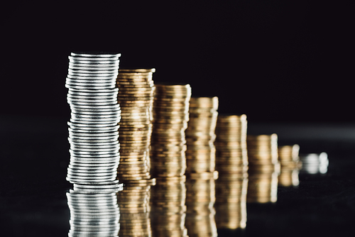 selective focus of stacked silver and golden coins on surface with reflection isolated on black