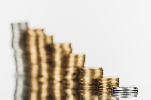 selective focus of stacked silver and golden coins on surface with reflection isolated on white