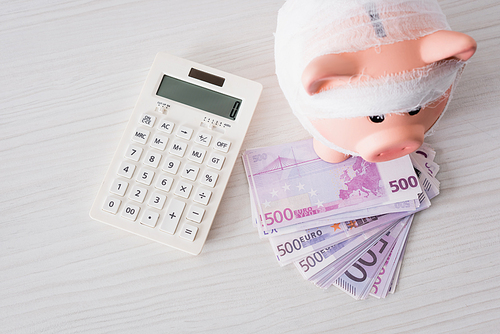 Top view of piggy bank with bandage on money near calculator