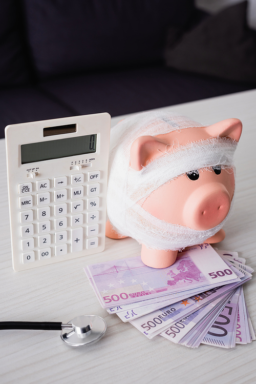 Selective focus of piggy bank with bandage on money near calculator