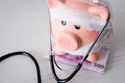 Selective focus of piggy bank on money with stethoscope on white table