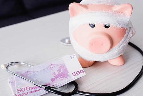 Selective focus of piggy bank near stethoscope and money on table