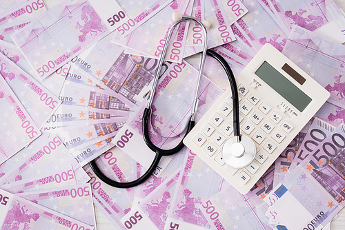 Top view of white calculator and stethoscope on euro banknotes