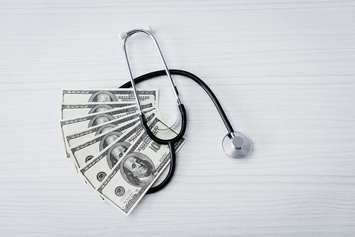 Top view of stethoscope and dollar banknotes on white table