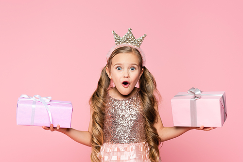 shocked little girl in crown holding wrapped presents isolated on pink