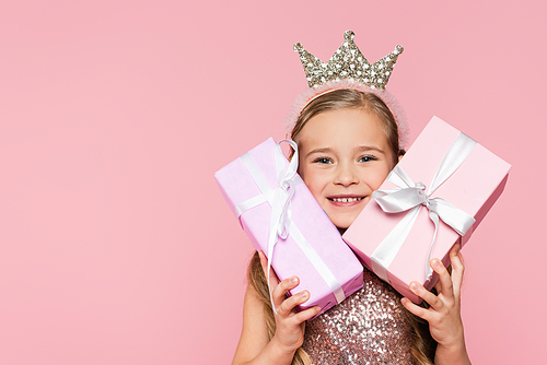 happy little girl in crown holding wrapped presents isolated on pink