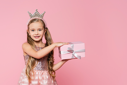 joyful little girl in crown holding wrapped present isolated on pink