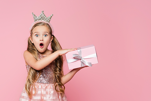 amazed little girl in crown holding wrapped present isolated on pink