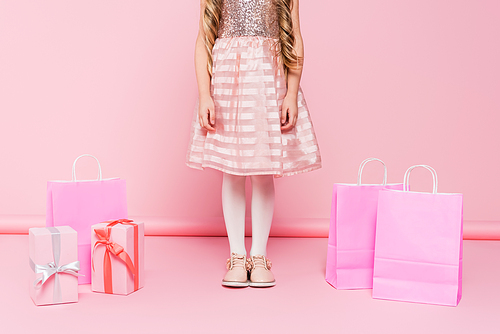 cropped view of little girl in dress standing near presents and shopping bags on pink